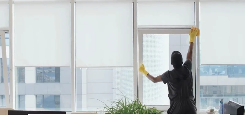 Cleaner in yellow gloves wiping a large window